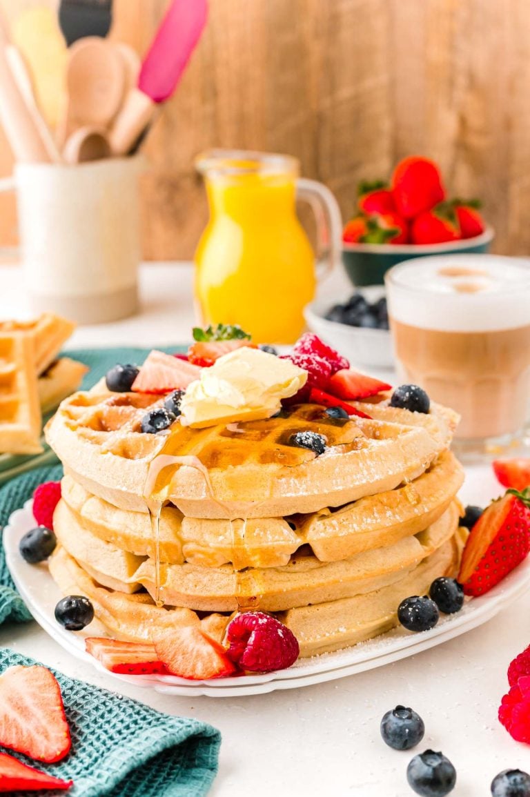 Close up photo of a woman pouring maple syrup over the top of a stack of Belgian waffles.