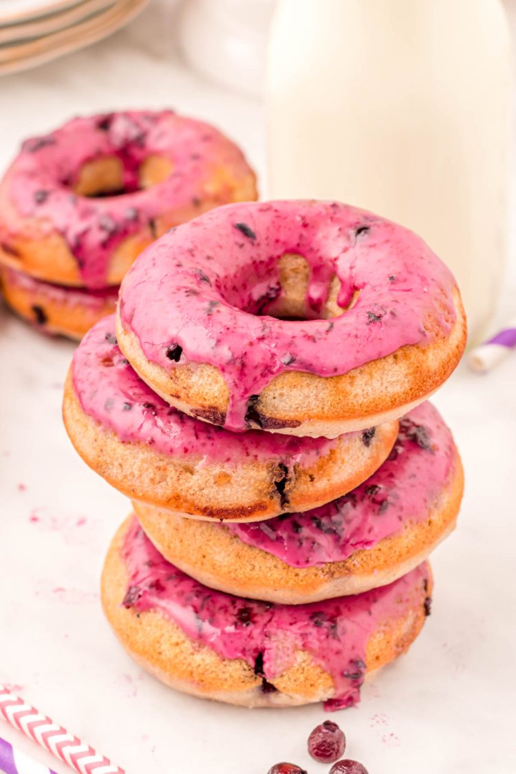 Close up photo of a stack of blueberry donuts on a white table with milk and donuts in the background.