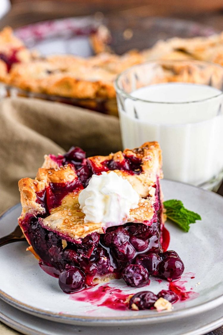 Close up photo of a slice of blueberry pie on a gray plate with a bite missing from it.