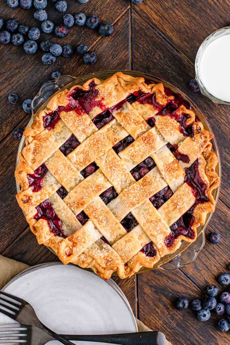 Overhead photo of a blueberry pie with a lattice crust on a wooden table.