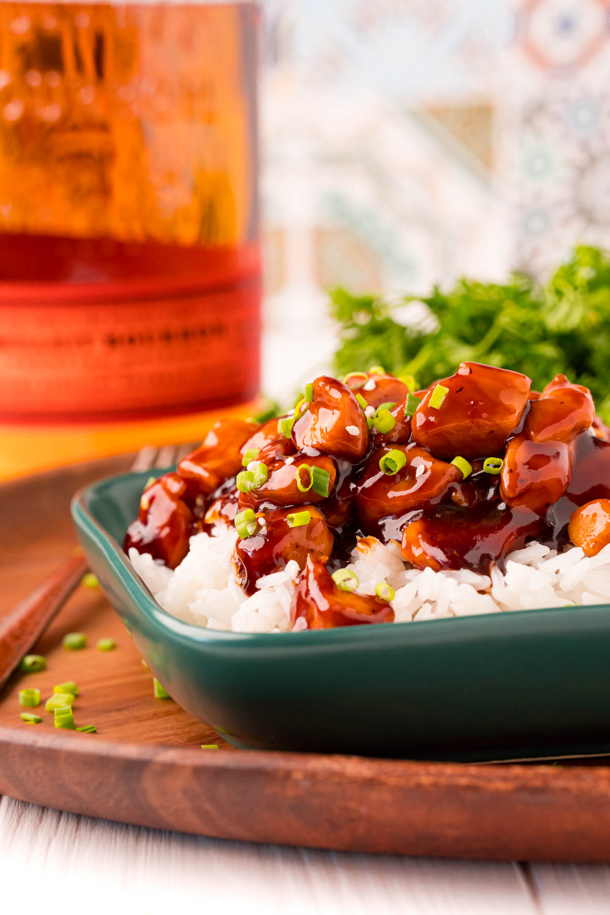 Close up photo of bourbon chicken and rice on a green plate on a wooden platter.