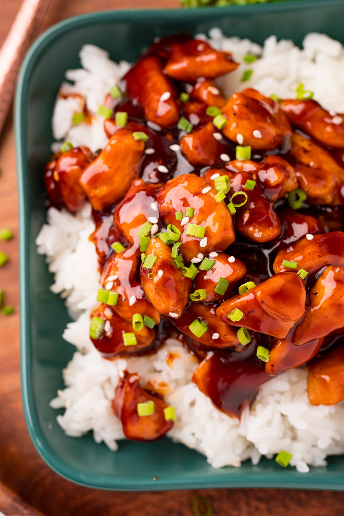 Close up photo of bourbon chicken on a bed of rice on a teal green dish.