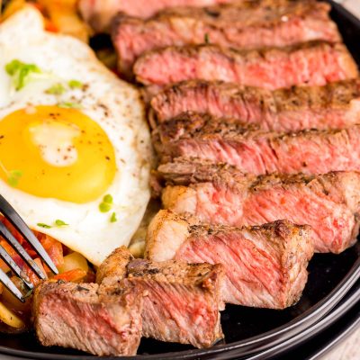 Close up photo of steak and eggs on a black plate.