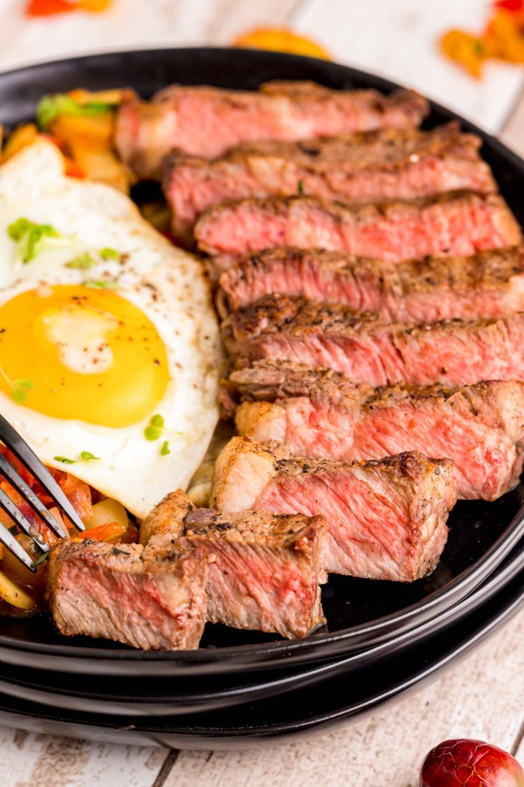 Close up photo of steak and eggs on a black plate.