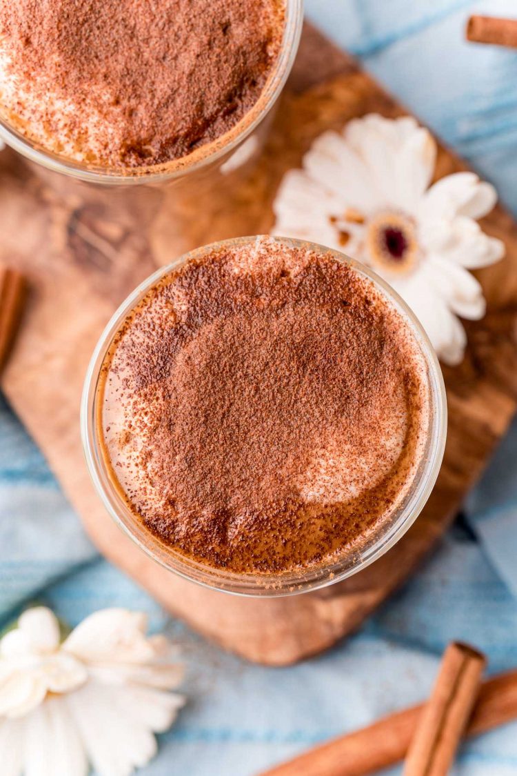 Overhead photo of cafe con miel on a wooden cutting board with cinnamon sticks and flowers around it.