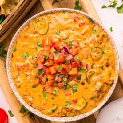 A bowl of smoked queso dip on a wooden cutting board.