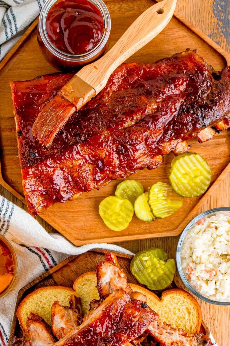 Overhead photo of ribs on a wooden plate with barbecue sauce and pickles.