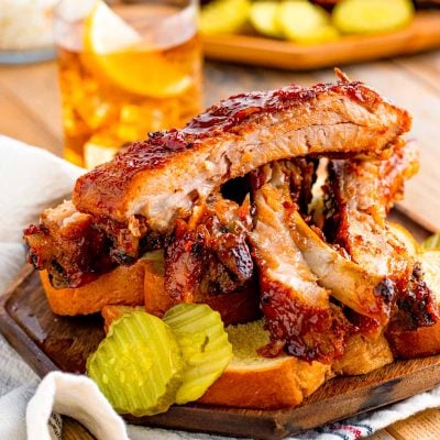 Close up photo of BBQ baby back ribs on a plate with bread and pickles.