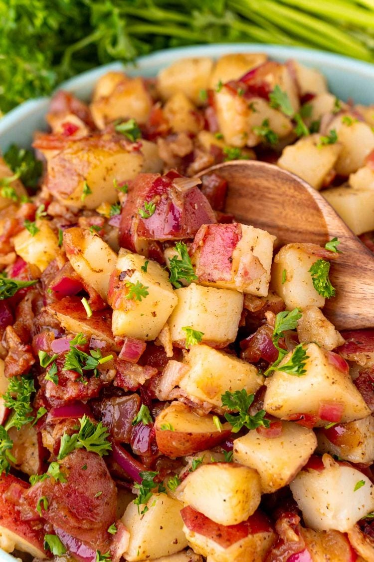 Close up photo of a bowl of German potato salad with a wooden spoon scooping some out.