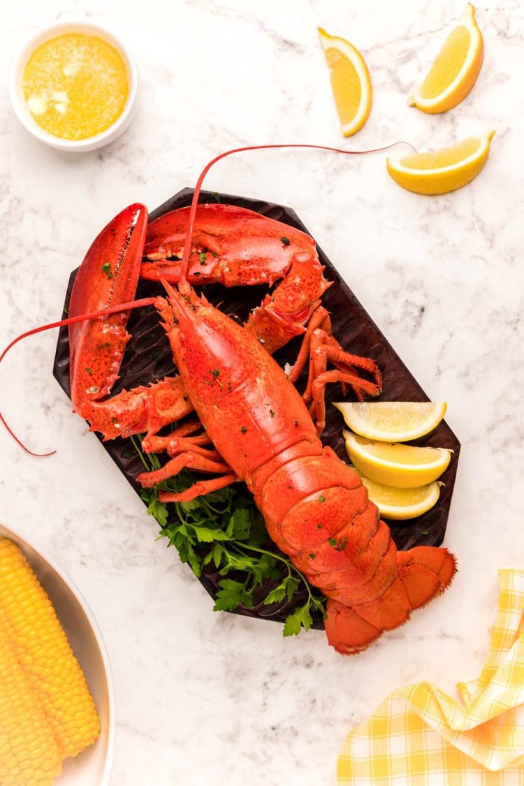 Overhead photo of a cooked lobster on a cutting board with lemon wedges and butter around it.