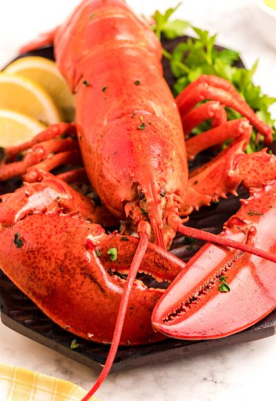 Close up photo of a cooked red lobster on a cutting board with herbs and lemon.