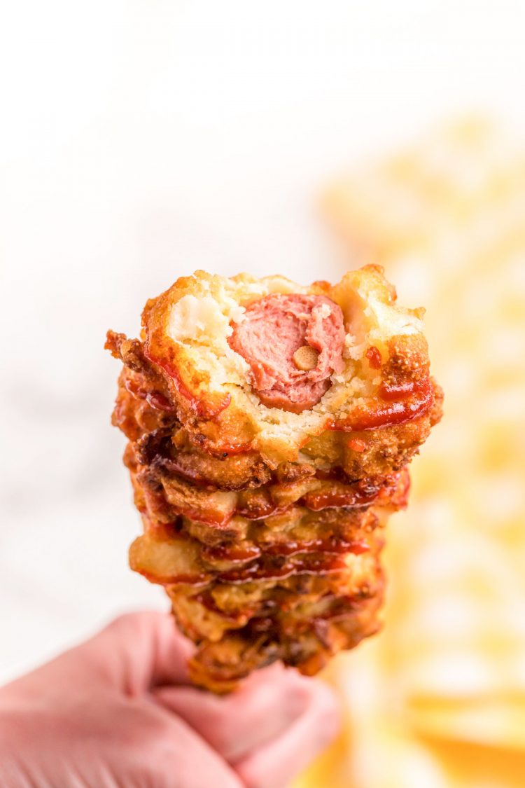 A woman's hand holding a Korean corndog with a bite taken out of it so you can see the hot dog inside.