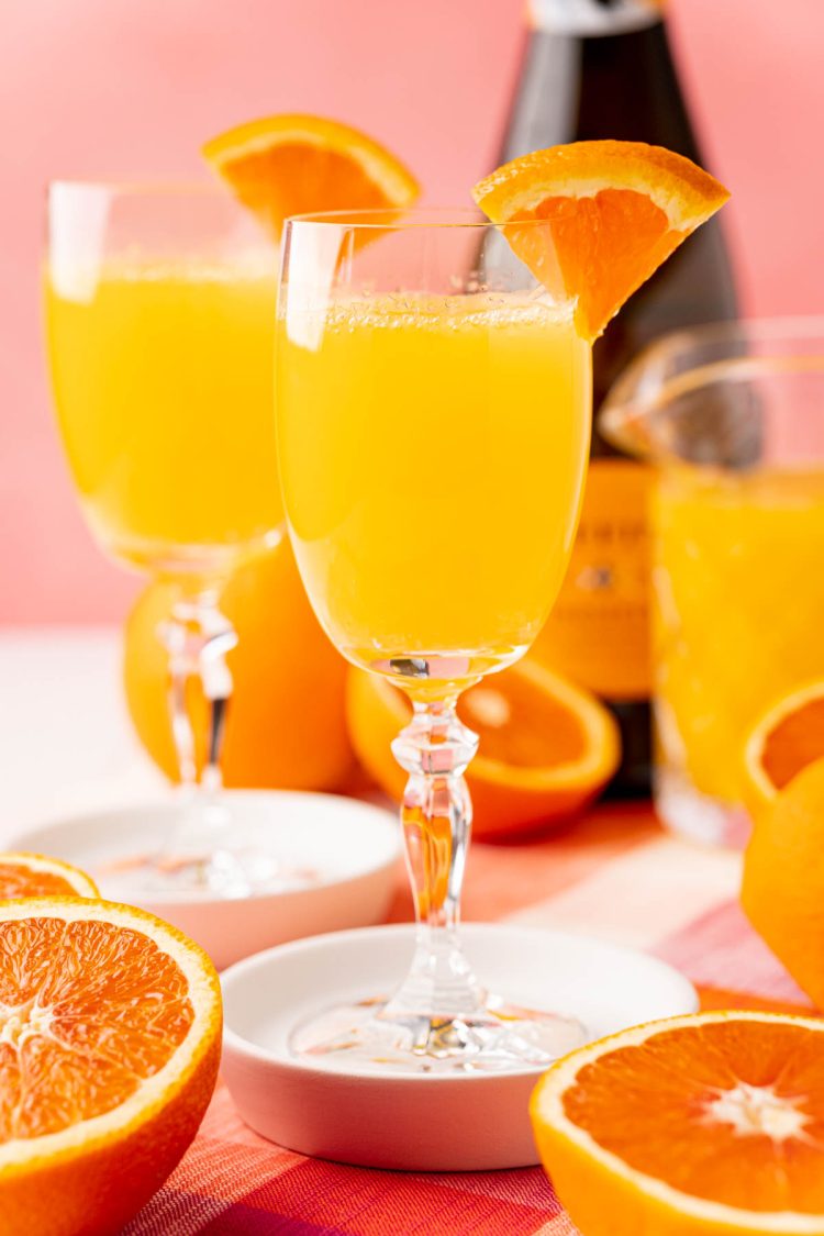 Close up photo of two mimosas on white coasters with sliced oranges around them.