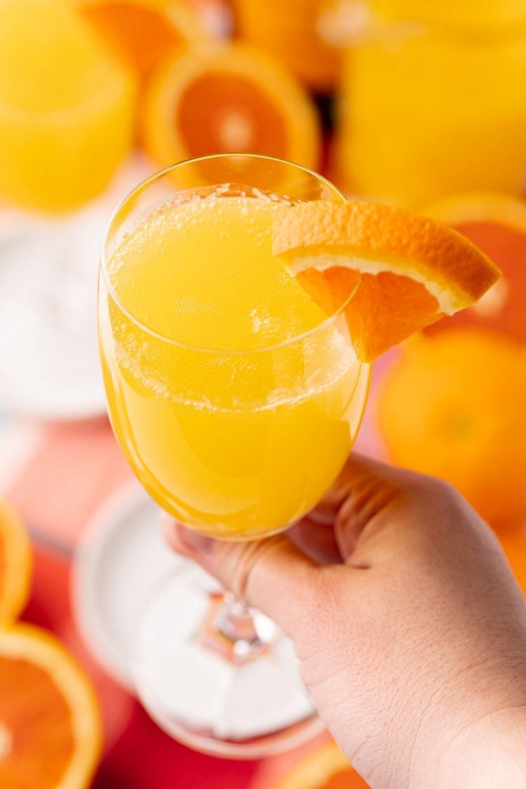 A woman's hand holding a mimosa to the camera.