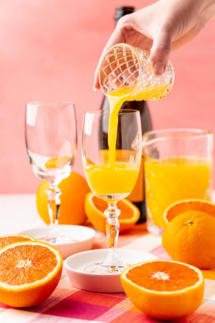 Orange juice being poured into a champagne flute to make a mimosa.