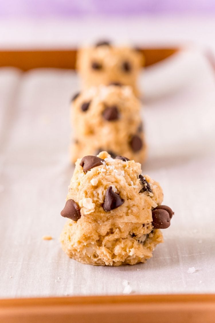 Close up photo of balls of cookie dough on a parchment lined baking sheet.