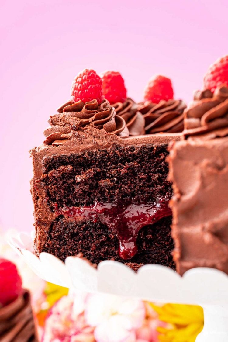 Close up photo of a chocolate cake with raspberry filling on a white cake stand.