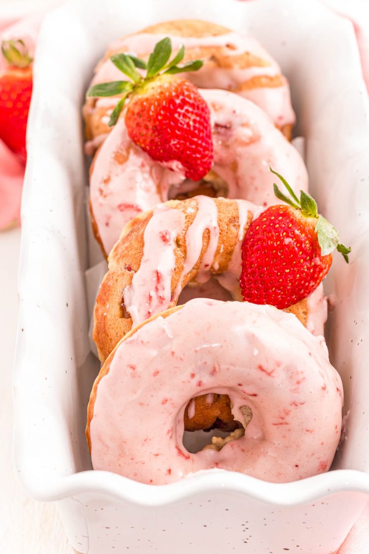 Strawberry donuts in a white serving dish with strawberries.