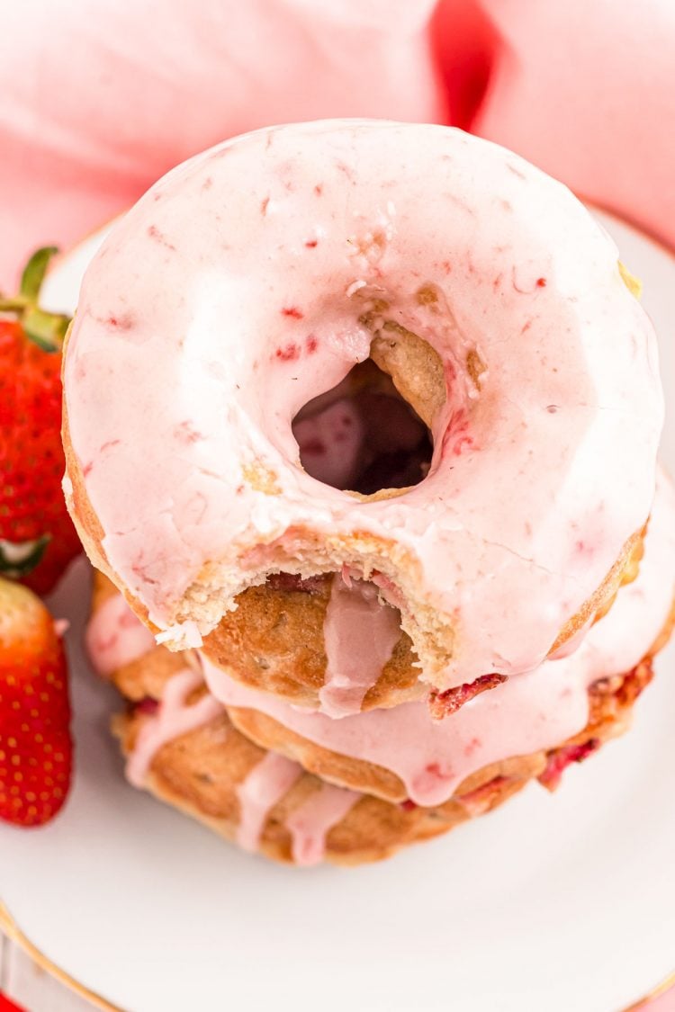 Close up angled photo of a stack of strawberry donuts on a white plate.