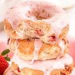 Close up photo of strawberry donuts stacked with the top one missing a bite.