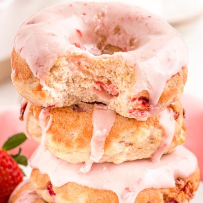 Close up photo of strawberry donuts stacked with the top one missing a bite.