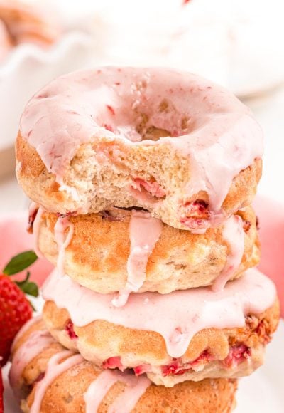 Close up photo of strawberry donuts stacked with the top one missing a bite.