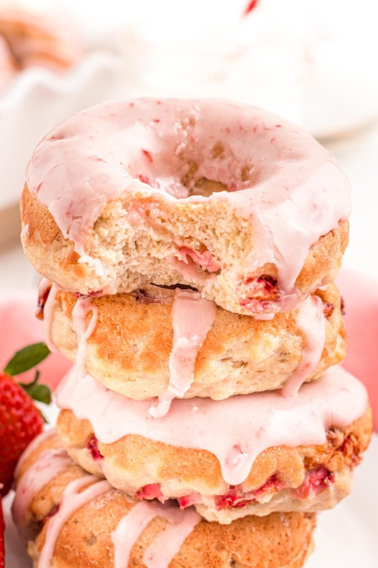 Close up photo of strawberry donuts stacked with the top one missing a bite.
