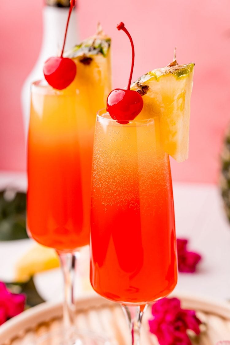 Close up photo of two Hawaiian Mimosas in champagne sluted garnished with pineapple wedges and cherries.