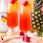 Close up photo of two Hawaiian Mimosas in champagne sluted garnished with pineapple wedges and cherries.