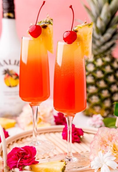 Close up photo of two Hawaiian Mimosas in champagne sluted garnished with pineapple wedges and cherries.