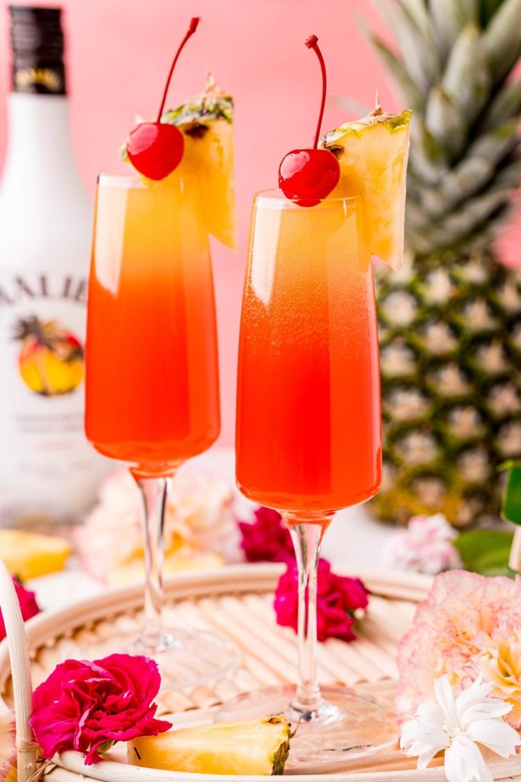 Close up photo of two Hawaiian Mimosas in champagne sluted garnished with pineapple wedges and cherries.