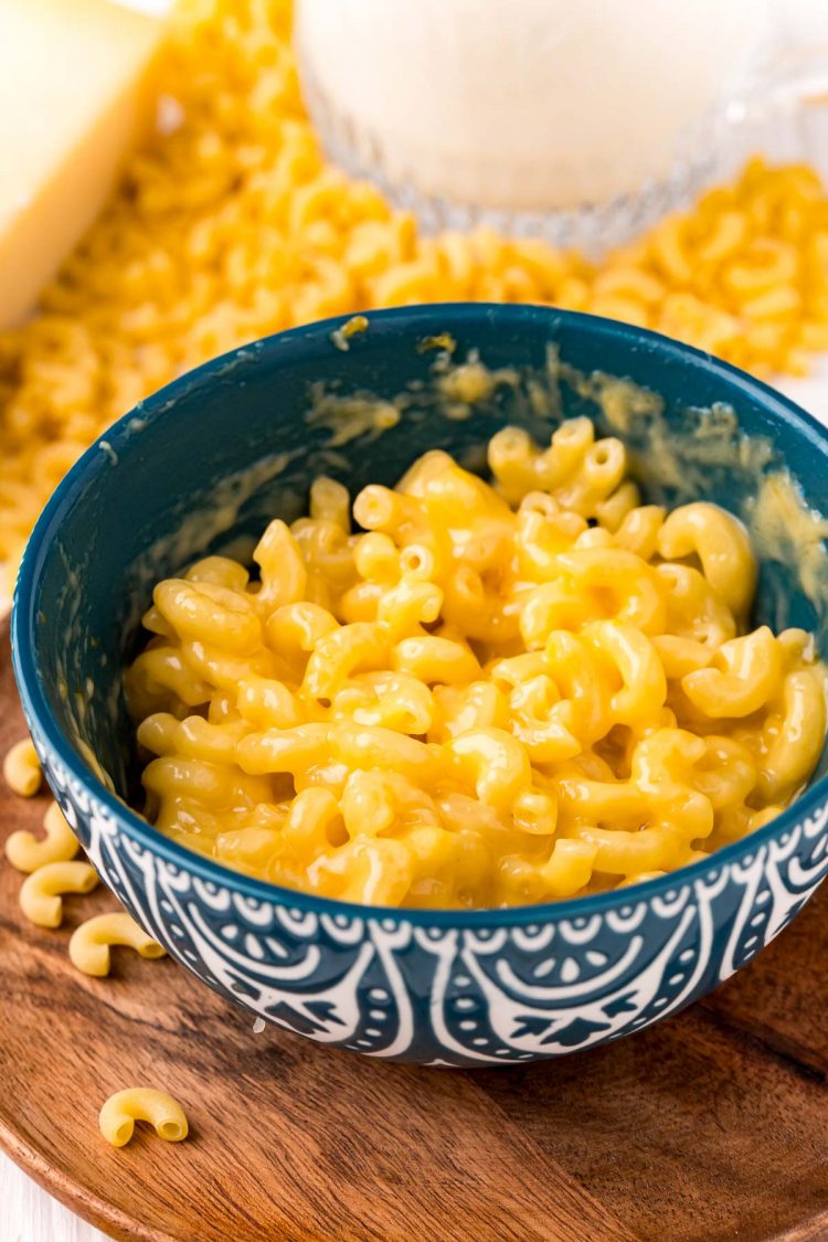 Close up photo of mac and cheese in a teal mug on a wooden plate.