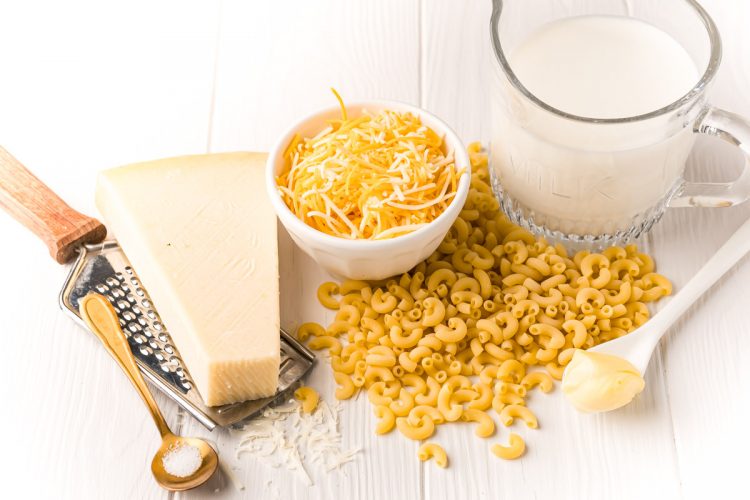 Ingredients to make mac and cheese in a mug on a white wooden table.