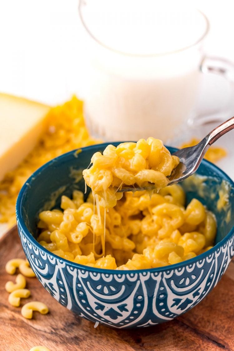 A fork scooping a bite of mac and cheese out of a blue mug.