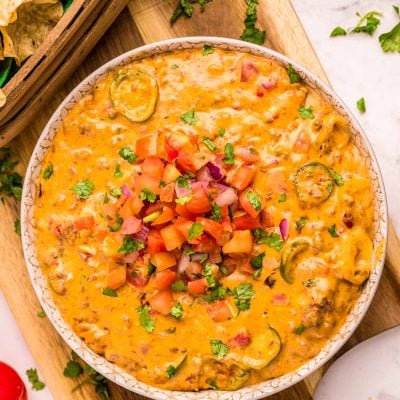 A bowl of smoked queso dip on a wooden cutting board.