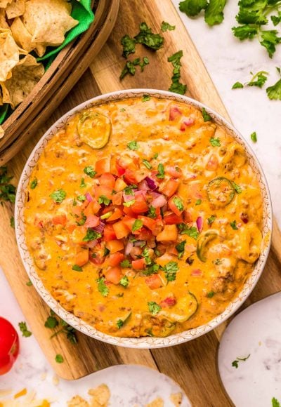 A bowl of smoked queso dip on a wooden cutting board.