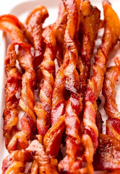 Close up photo of twisted bacon on a white serving tray.