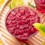 Close up photo of a woo woo cocktail garnished with lime on a wooden tray.