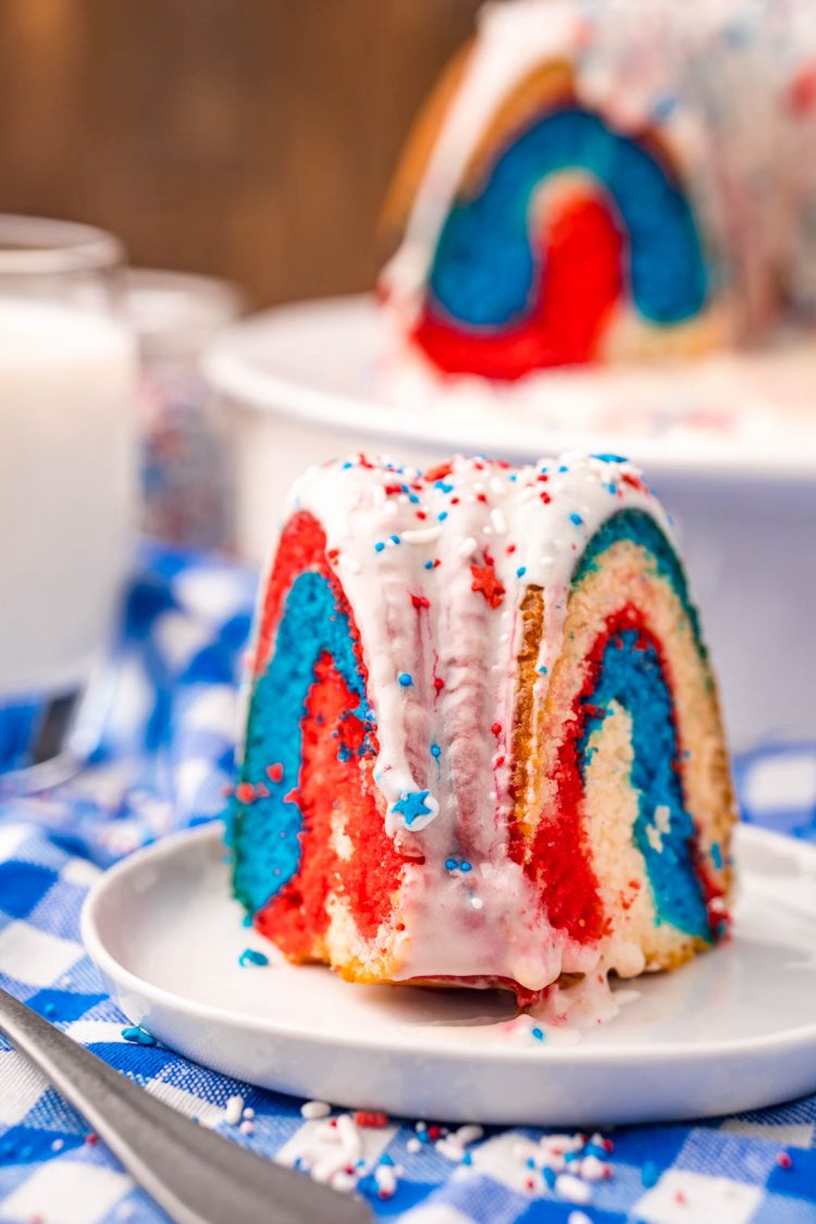 Close up photo of a slice of 4th of july bundt cake on a white plate on a blue gingham napkin.