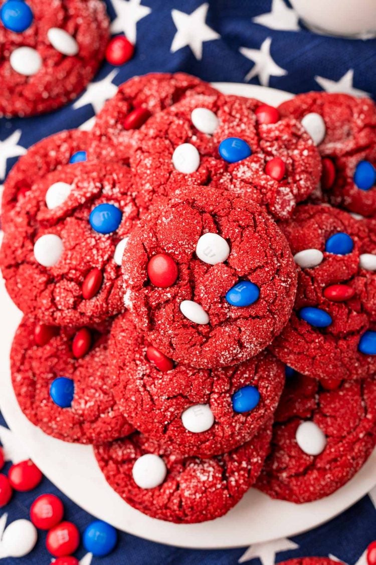 Overhead photo of red velvet cake mix cookies with red, white, and blue M&M's on a white plate on a blue star napkin.