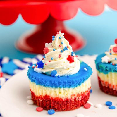 Close up photo of 4th of July mini cheesecakes on a white plate with sprinkles around them.