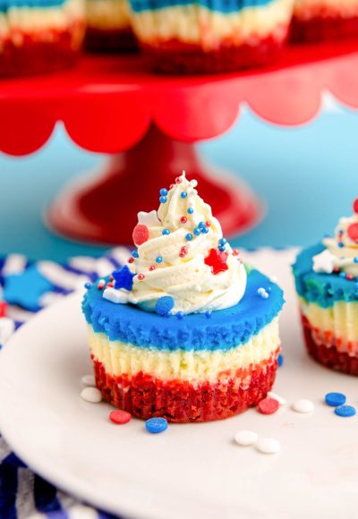 Close up photo of 4th of July mini cheesecakes on a white plate with sprinkles around them.