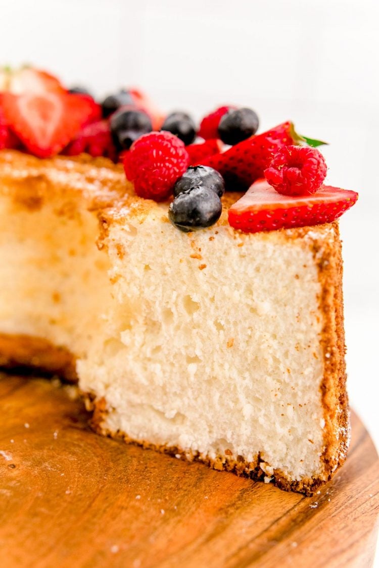 Close up photo of angel food cake on a wooden cake stand with a slice missing.