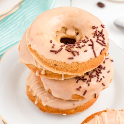 Close up photo of coffee donuts stacked on top of each other on a white plate.