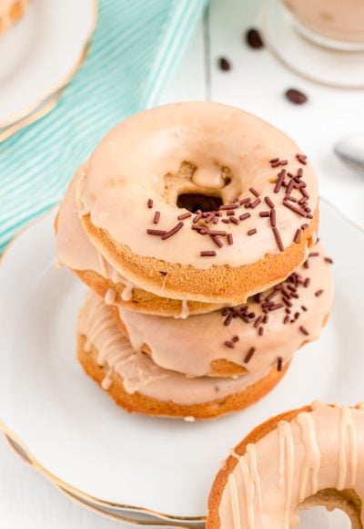 Close up photo of coffee donuts stacked on top of each other on a white plate.