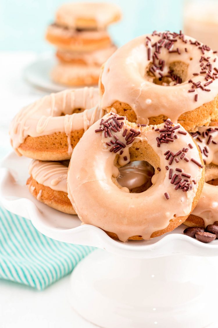 Close up photo of coffee donuts on a white cake stand with a teal napkin in the background.