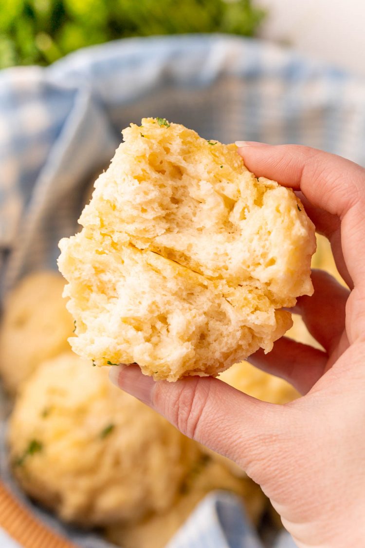 A woman's hand holding a drop biscuit that has been broken in half to show the texture.