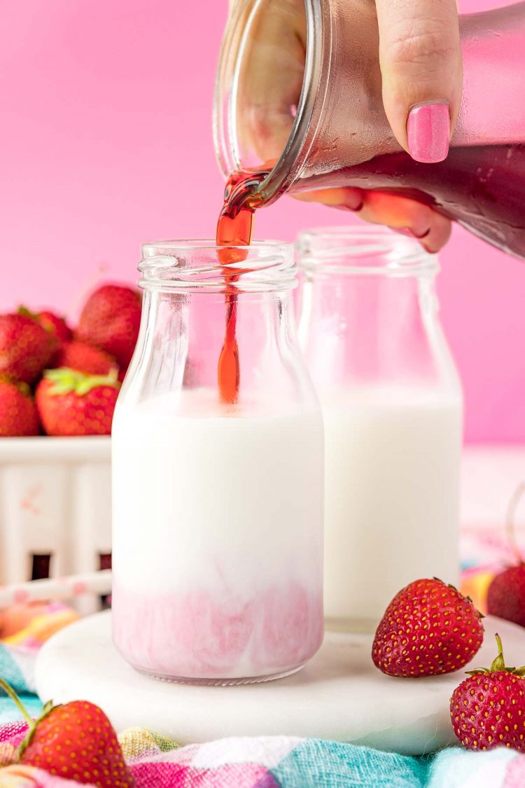 Strawberry simple syrup being poured into a bottle of milk.