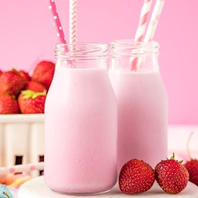 Close up photo of two milk bottles of homemade strawberry milk on a white board.