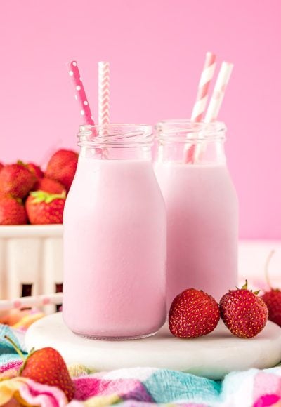 Close up photo of two milk bottles of homemade strawberry milk on a white board.